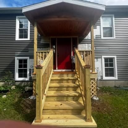 A new wooden staircase and porch with a red door on the front of a house with grey siding.