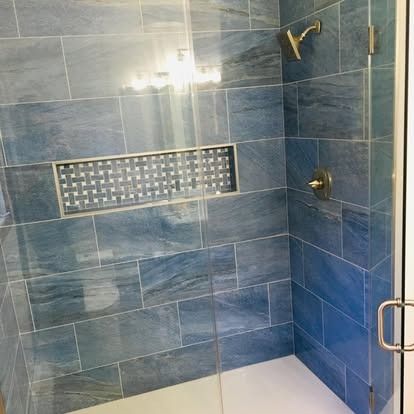 A glass-enclosed shower with blue, marble-patterned tiles and a rectangular niche featuring metallic, basket-weave tile.