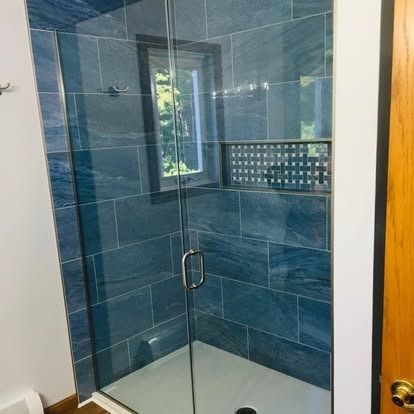 A modern shower stall featuring blue, rectangular stone-look tiles, a glass door, and a built-in recessed shelf.
