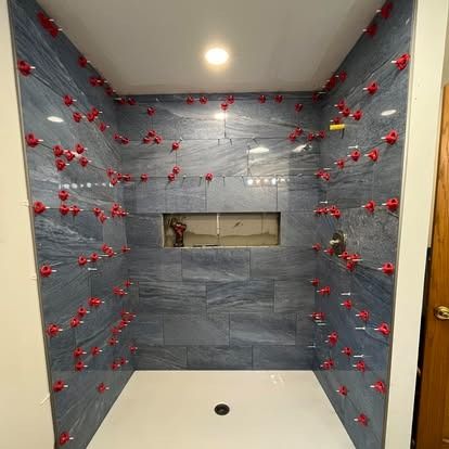 A shower stall under construction with blue stone-look tiles and red leveling clips still attached to the walls.