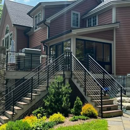 A multi-level wood deck with black metal railing and stairs leading down to a landscape garden by a brown house.