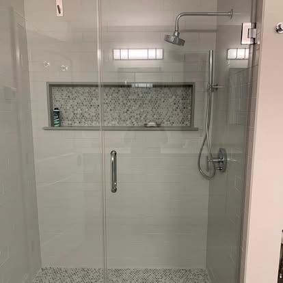 A modern glass-enclosed shower with white subway tile walls, a patterned tile recessed niche, and chrome fixtures.