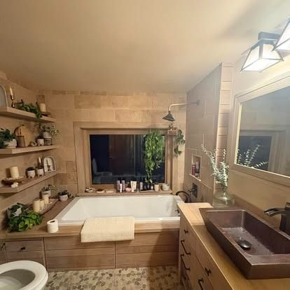 A bathroom features a soaking tub, floating wood shelves with decor, a stone vessel sink, and beige tile walls.