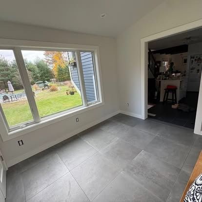 A sunroom with gray tile flooring, white walls, and a large window looking out onto a green backyard and patio.