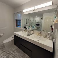 A modern bathroom features a dark vanity with a white countertop, a large mirror with a linear light, and tiled flooring.