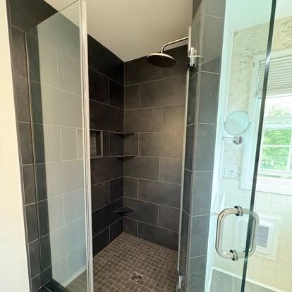 A walk-in shower with dark gray rectangular tiles, a rainfall showerhead, and a glass door with a silver handle.