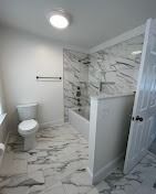 A bathroom featuring white walls, marble-patterned tile flooring, a white toilet, and a bathtub with matching tiled walls.