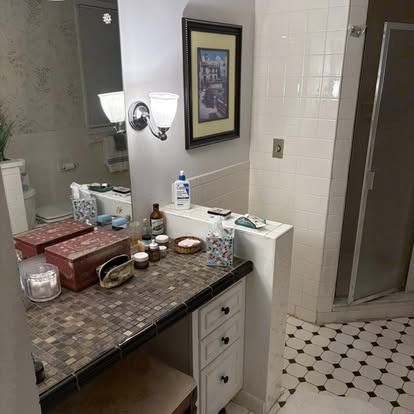 A bathroom vanity with a tiled countertop, two red boxes, toiletries, and a framed picture on the wall above the sink.