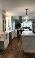 A bright kitchen with white cabinetry, a center island, dark wood floors, and a pendant light fixture over the sink area.