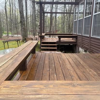 A multi-level stained wooden deck featuring built-in bench seating and stairs, set against a wooded background.