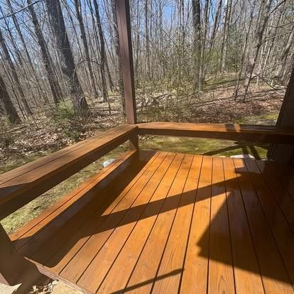 A wooden deck with built-in benches overlooks a wooded area with trees and a mossy ground.