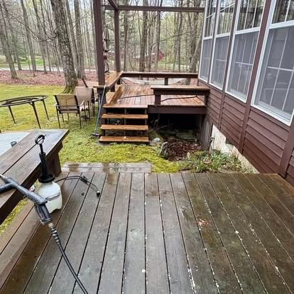 A pressure washer wand lies on a wooden deck next to steps leading to a raised deck against a house in a wooded yard.