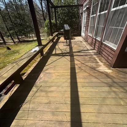 A wooden deck with a built-in bench, a grill in the distance, and a long shadow cast across the boards on a sunny day.