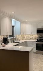 Modern kitchen with white cabinets, light quartz countertops, and a textured stone tile backsplash.