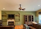 A living room with green built-in shelves surrounding a fireplace, hardwood floors, a ceiling fan, and brown furniture.