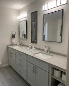 A modern double-sink bathroom vanity with light gray cabinets, white countertops, two mirrors, and overhead lighting.