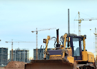 A yellow bulldozer sits in the foreground of a construction site with several tall tower cranes and apartment buildings.