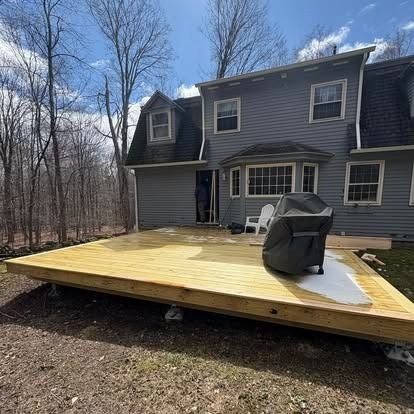 A newly built, light-wood deck sits against a gray two-story house with a partially visible person standing in the doorway.