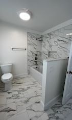 A modern bathroom featuring a white toilet, marble-patterned tile floors, and a walk-in shower with marble-tiled walls.