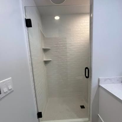 A modern glass walk-in shower with white subway tile walls, built-in corner shelves, and black hardware.
