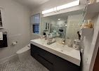 A modern bathroom featuring a dark grey floating vanity, white countertop, large mirror, and grey patterned tile floor.