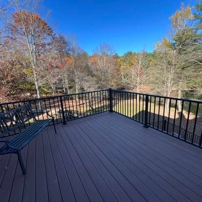 A deck with brown composite boards and a black railing overlooking a yard with autumn trees under a clear blue sky.