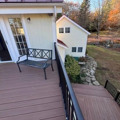A view from a wooden deck looking down at a flagstone path, a small cream-colored building, and a wooded yard.