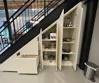 Custom white storage cabinets built into the alcove underneath an indoor staircase.