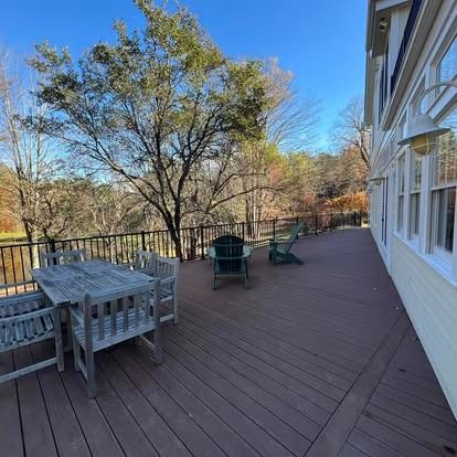 A large wooden deck with outdoor table and chair sets, overlooking a forested landscape under a clear blue sky.