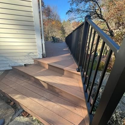 Composite deck steps leading to a landing with a black railing, set against a house exterior on a sunny day.