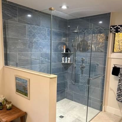 A glass-enclosed shower with gray rectangular tile walls, a built-in corner shelf, and chrome fixtures.