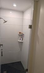 A modern walk-in shower with white tiled walls, a glass door, a silver showerhead, and a two-tier corner shelving unit.