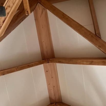 A low-angle view of a white vaulted ceiling featuring exposed wooden support beams arranged in a corner structure.