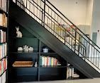 Black staircase with open shelving built underneath, displaying books, decorative items, and a small cat figurine.