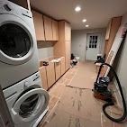A laundry room under renovation with a stacked washer and dryer, unfinished wooden cabinets, and protective floor paper.