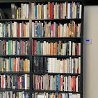 A tall, black bookshelf filled with many colorful books, with a digital thermostat mounted on the adjacent wall.