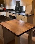 A kitchen view featuring a wood-topped breakfast bar in the foreground and white cabinets with black counters behind.