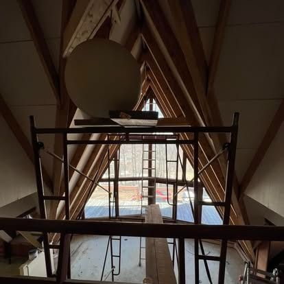 A metal scaffolding frame stands inside an A-frame building under construction, looking out toward an exterior view.