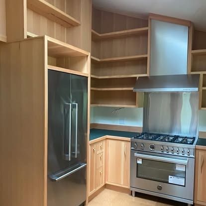 A modern kitchen featuring light wood cabinetry, open shelving, a stainless steel refrigerator, and a gas stove.