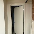 An open white door in a white frame, with a dark room visible behind it and a brick wall on the right.