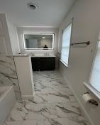 Modern bathroom with marble-look tile floors, a dark vanity, a backlit mirror, and a window with white blinds.