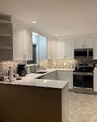 Modern kitchen featuring white cabinets, stone backsplash, stainless steel appliances, and a quartz countertop peninsula.
