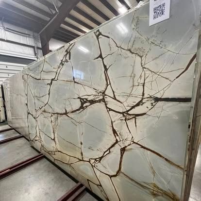 Large, polished slab of white and pale green stone with bold, dark brown, vein-like fractures, displayed in a warehouse.