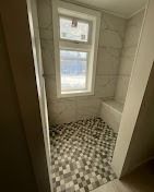 A shower area featuring a window, light-colored tiled walls, and a small, checkered floor pattern.