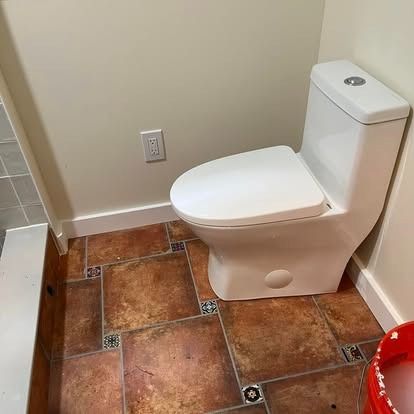 A modern white toilet in a bathroom with mottled brown tile flooring and cream-colored walls.