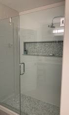A modern glass-enclosed shower with white subway tile walls, a mosaic-tiled recessed shelf, and a pebble-tiled floor.