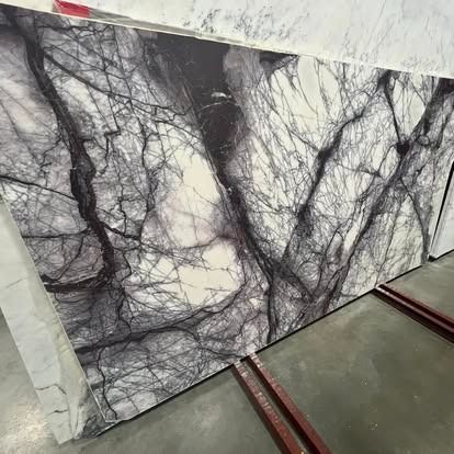 A large slab of white marble featuring dramatic, sprawling deep purple and black veins, resting on metal supports.