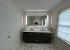 A modern bathroom featuring a dark wood double-sink vanity, a large rectangular lighted mirror, and herringbone flooring.