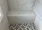 A tiled shower bench with marble-look surfaces and a checkered floor pattern.