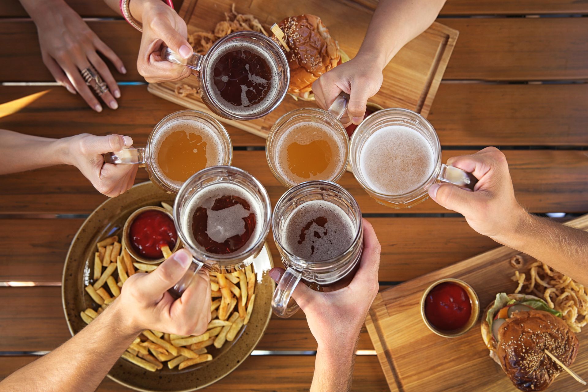 A group of people enjoy a diverse spread of food at a wooden table, featuring burgers, tacos, and steaks.